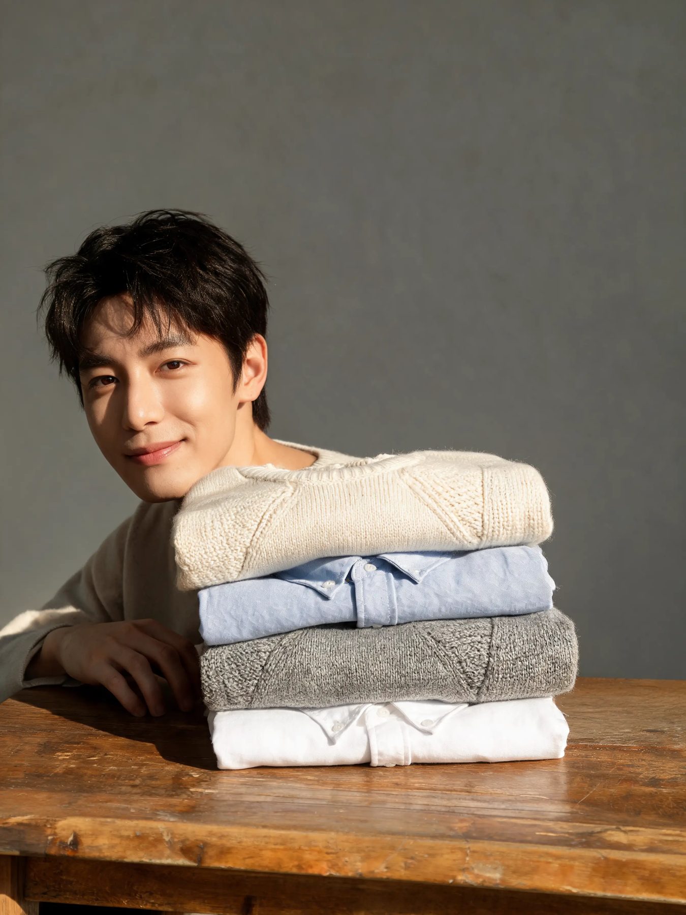 Folded knitwear and shirts stacked on a worn oak table